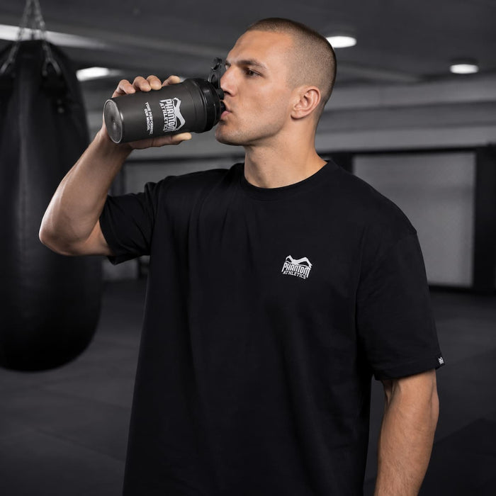 Kampfsport-Athlet mit Phantom Athletics Oversize T-Shirt und Shaker beim Trinken nach dem Training