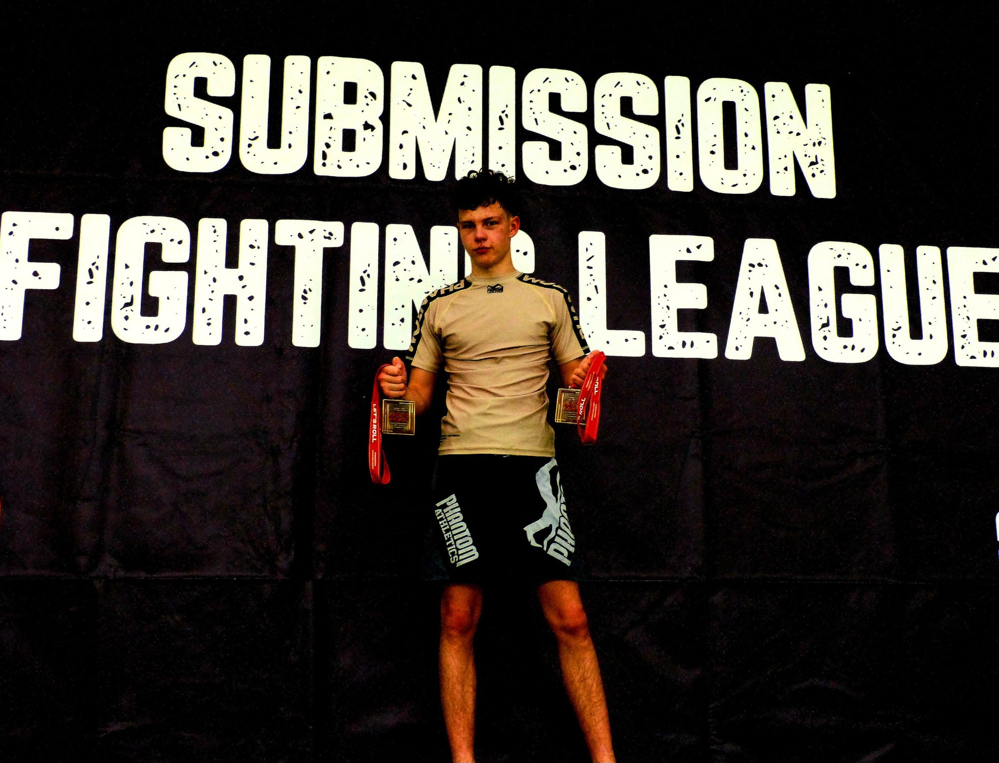 MMA-Fighter Jonas "Chokemon" Dornhofer mit Phantom Athletics T-Shirt, Training Shorts und Medaillen nach einem Kampf