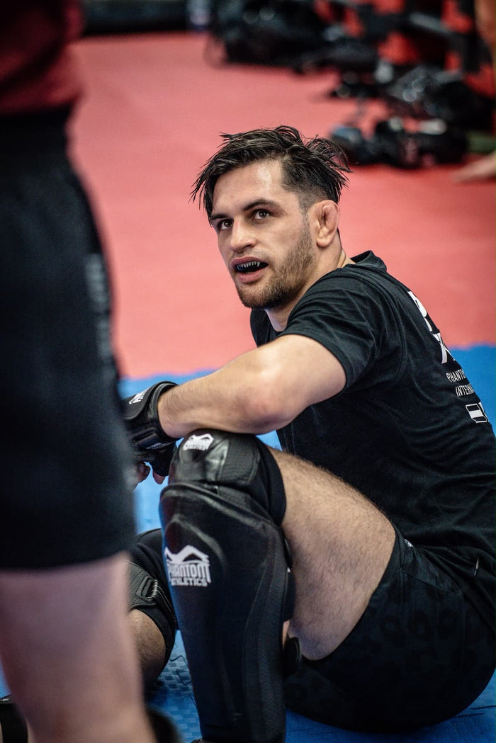 MMA-Fighter Nikolaos Serbezis mit Phantom Athletics T-Shirt, Fight Shorts, Knieschutz, Schienbeinschutz und MMA-Handschuhen nach dem Training