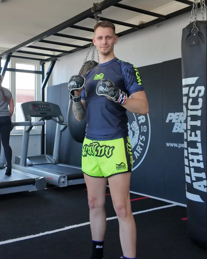 Muay Thai Fighter Michael Block mit Phantom Athletics MMA Sparring Handschuhe Sak Yant, Muay Thai Fight Shorts und Muay Thai Rashguard im Gym mit Phantom Athletics Boxsack im Hintergrund