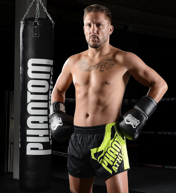Kampfsport-Athlet mit Phantom Athletics Training Shorts und Boxhandschuhen vor dem Boxsack High Performance