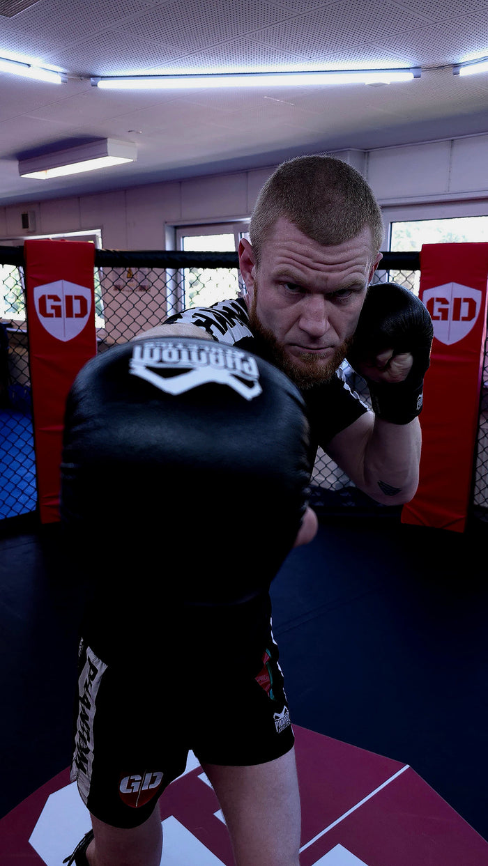 MMA-Fighter Simon Seiler mit Phantom Athletics T-Shirt, Training Shorts und MMA Gloves im Käfig
