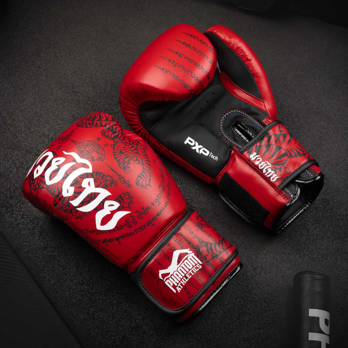 Die Phantom Muay Thai Boxhandschuhe in Top Qualität mit thailändischem Print in der Farbe Rot am Gymboden.