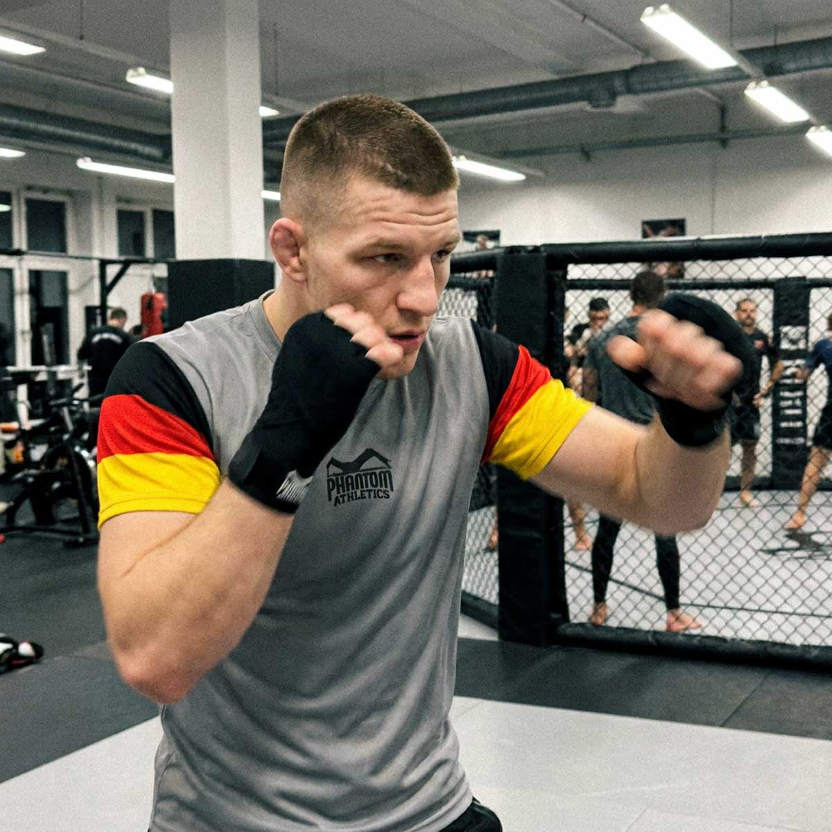 Mit dem Phantom Athletics Training Shirt EVO Team Germany Gray setzt du auf hochwertige Kampfsportbekleidung für anspruchsvolle Athleten. Das funktionelle Material eignet sich ideal für Boxtraining, Muay Thai und Sparring und unterstützt dich zuverlässig bei jeder Trainingseinheit.