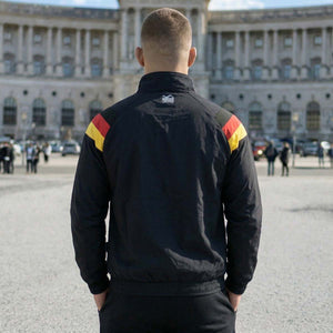 Die Phantom Athletics Trackjacket DMC Team Germany kombiniert klassischen Retro-Style in Schwarz/Rot/Gold mit moderner Performance für intensives Kampfsport-Training wie MMA, Boxen und Kickboxen. Das leichte, atmungsaktive Material mit Mesh-Innenfutter sorgt für optimalen Komfort und maximale Bewegungsfreiheit beim Warm-up und Sparring.
