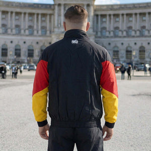Die Phantom Athletics Trackjacket DMC Team Germany vereint sportliches Design in Schwarz/Rot/Gold mit hochwertiger Performance für intensives Kampfsport-Training wie MMA, Boxen und Kickboxen. Das leichte, atmungsaktive Material mit Mesh-Innenfutter sorgt für optimalen Komfort und maximale Bewegungsfreiheit beim Sparring und Warm-up.
