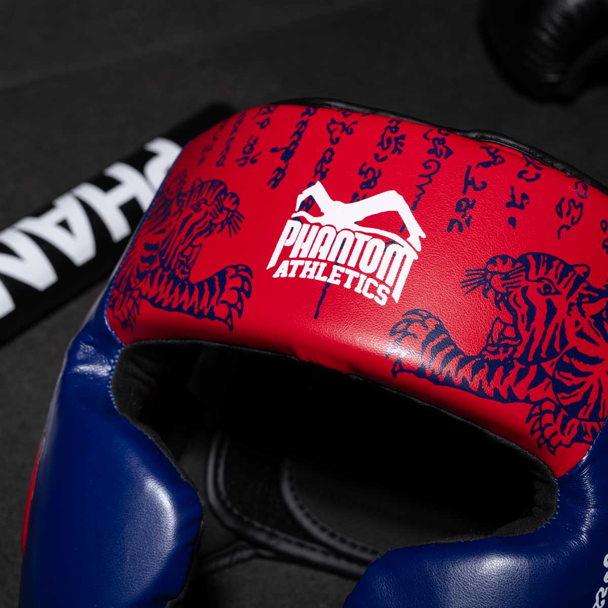 Phantom Muay Thai Kopfschutz für Thaiboxen und MMA Sparring, Wettkampf und Training. Im traditionellen Sak Yant Design und der Farbe Blau/Rot.