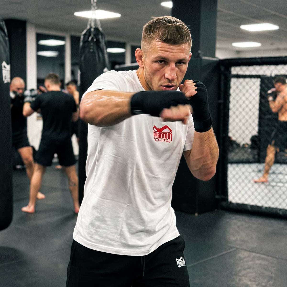 Das Phantom Athletics Team T-Shirt in Weiß verbindet einen cleanen Look mit einem markanten roten Logo und dezentem Branding im Nacken. Die hochwertige Fightwear ist ideal für Kampfsport, Functional Fitness, Gym und Freizeit.