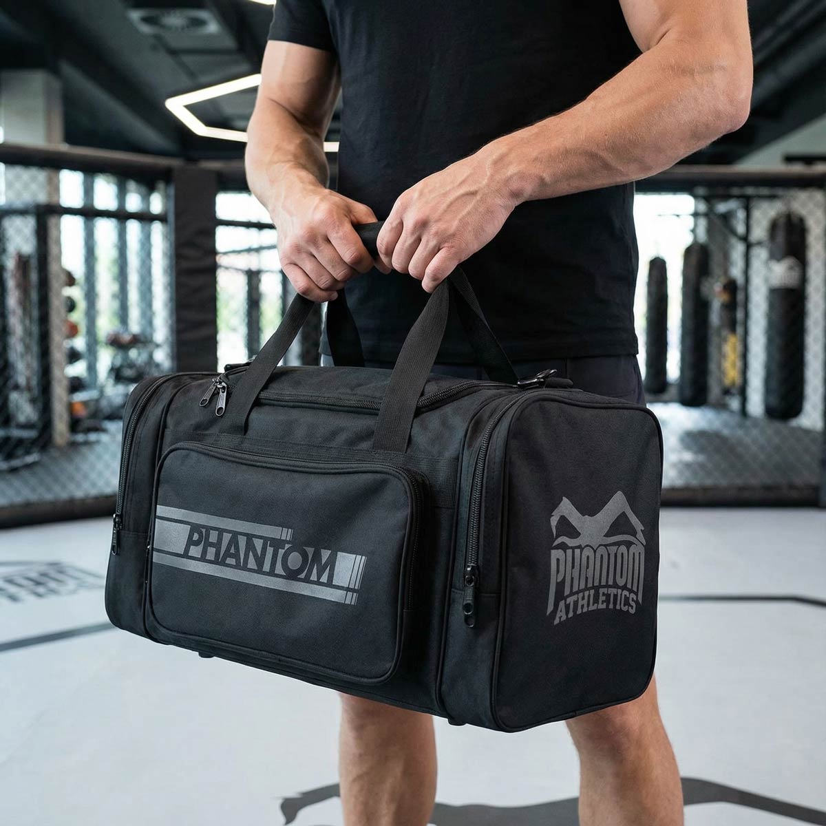 Robuste Phantom Athletics Kampfsport-Trainingstasche in Schwarz/Grau mit großem Volumen und zahlreichen Fächern, ideal zum Verstauen von Boxhandschuhen, Schienbeinschonern und Trainingszubehör für MMA, Muay Thai oder Kickboxen. Hergestellt aus widerstandsfähigem 1000D Nylon mit langlebigen Reißverschlüssen für den täglichen Einsatz im Gym. Diese Premium-Sporttasche unterstützt dich beim organisierten Training und unterstreicht die hochwertige Qualität der Marke.