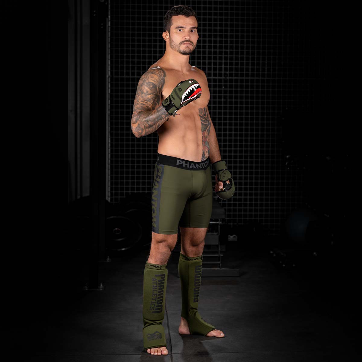 MMA Fighter im Gym mit den Army grünen MMA Sparringshandschuhen Fightsquad und mit grüner Phantom APEX Fightshorts und grünen Impact Schienbeinschonern